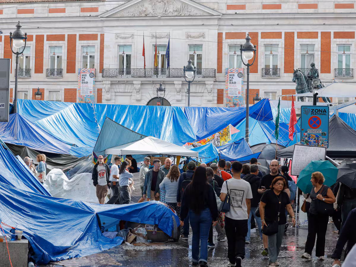 Una participante en la acampada de Puerta del Sol achica agua tras la fuerte lluvia caída en Madrid.